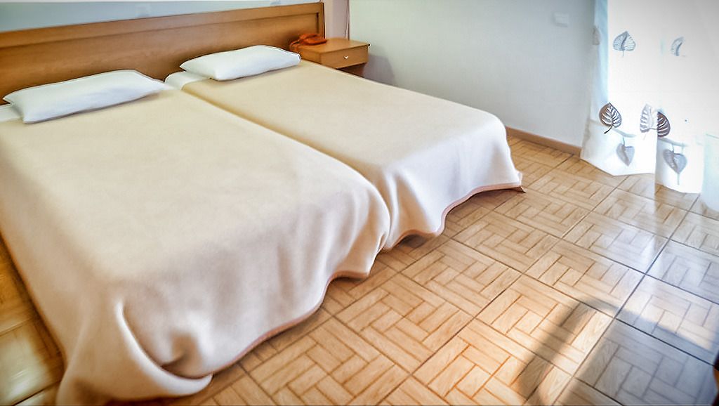 Ein Hotelzimmer mit zwei Betten, Holzboden, einem Nachttisch und einer Wand mit Blattdekorationen.