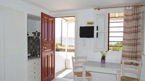 Ein Zimmer mit Esstisch, Stühlen, einem an der Wand montierten Fernseher und Blick ins Freie.