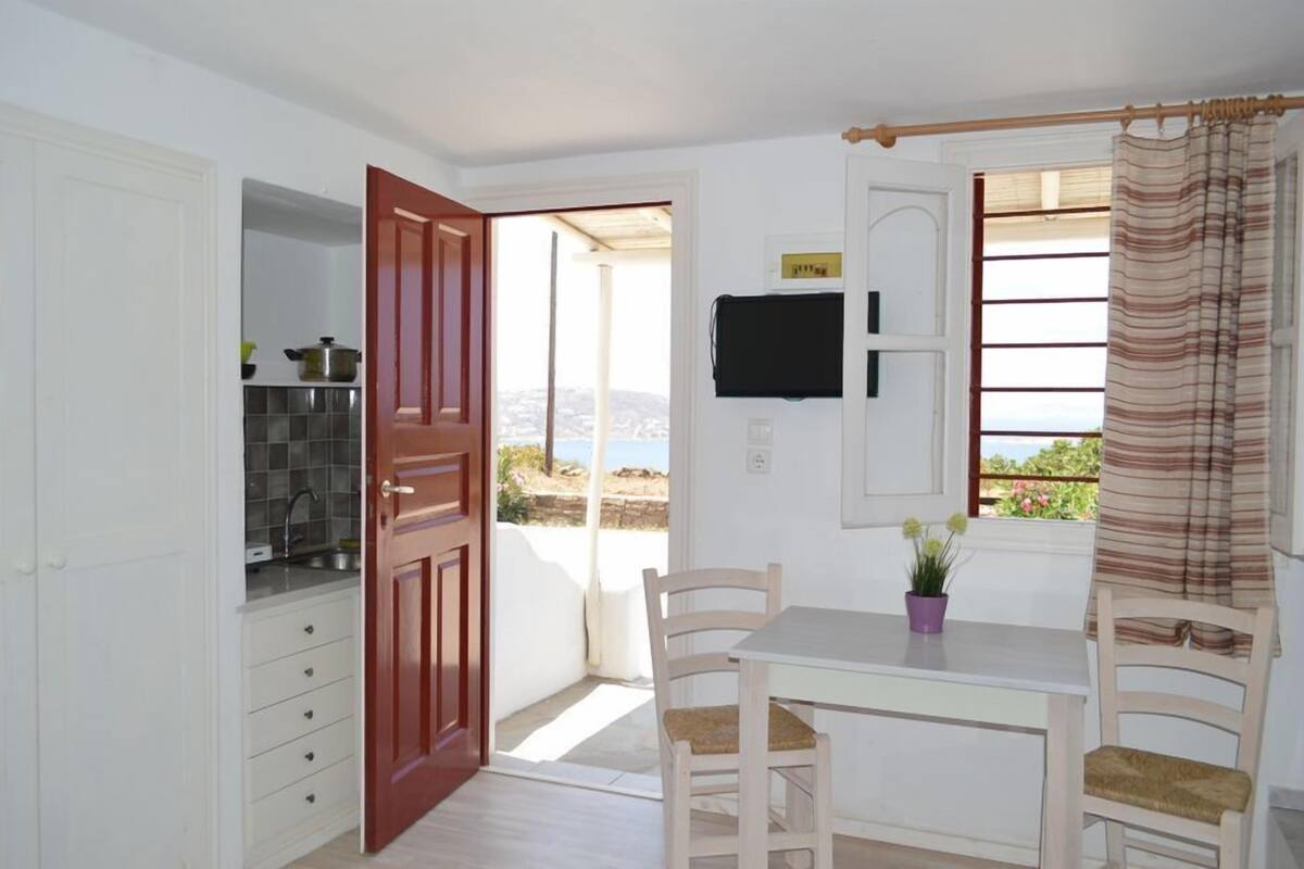 A room with a dining table, chairs, a TV mounted on the wall, and a view of the outdoors.