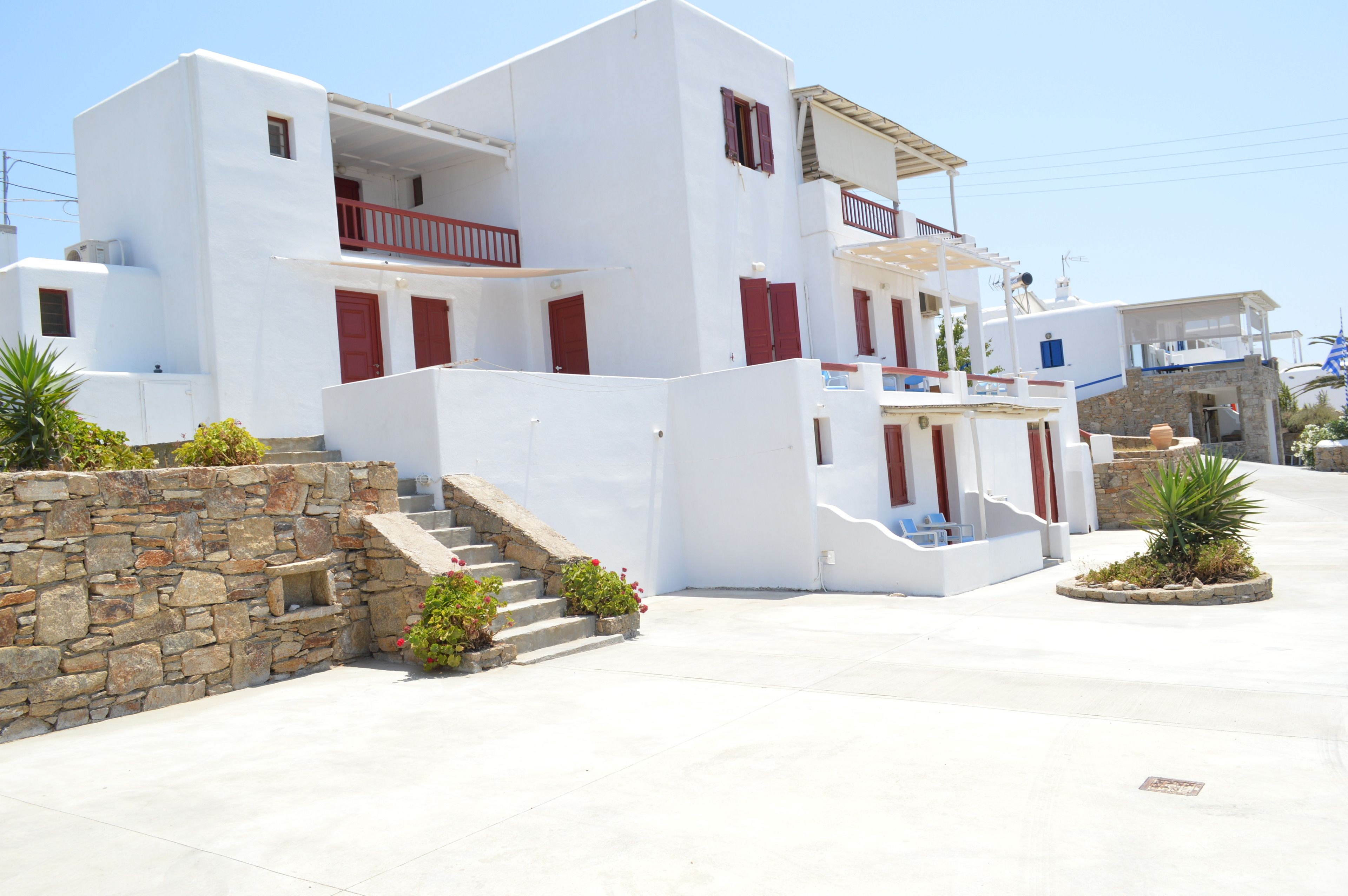 A white building with red shutters, a stone wall, and a small garden area.