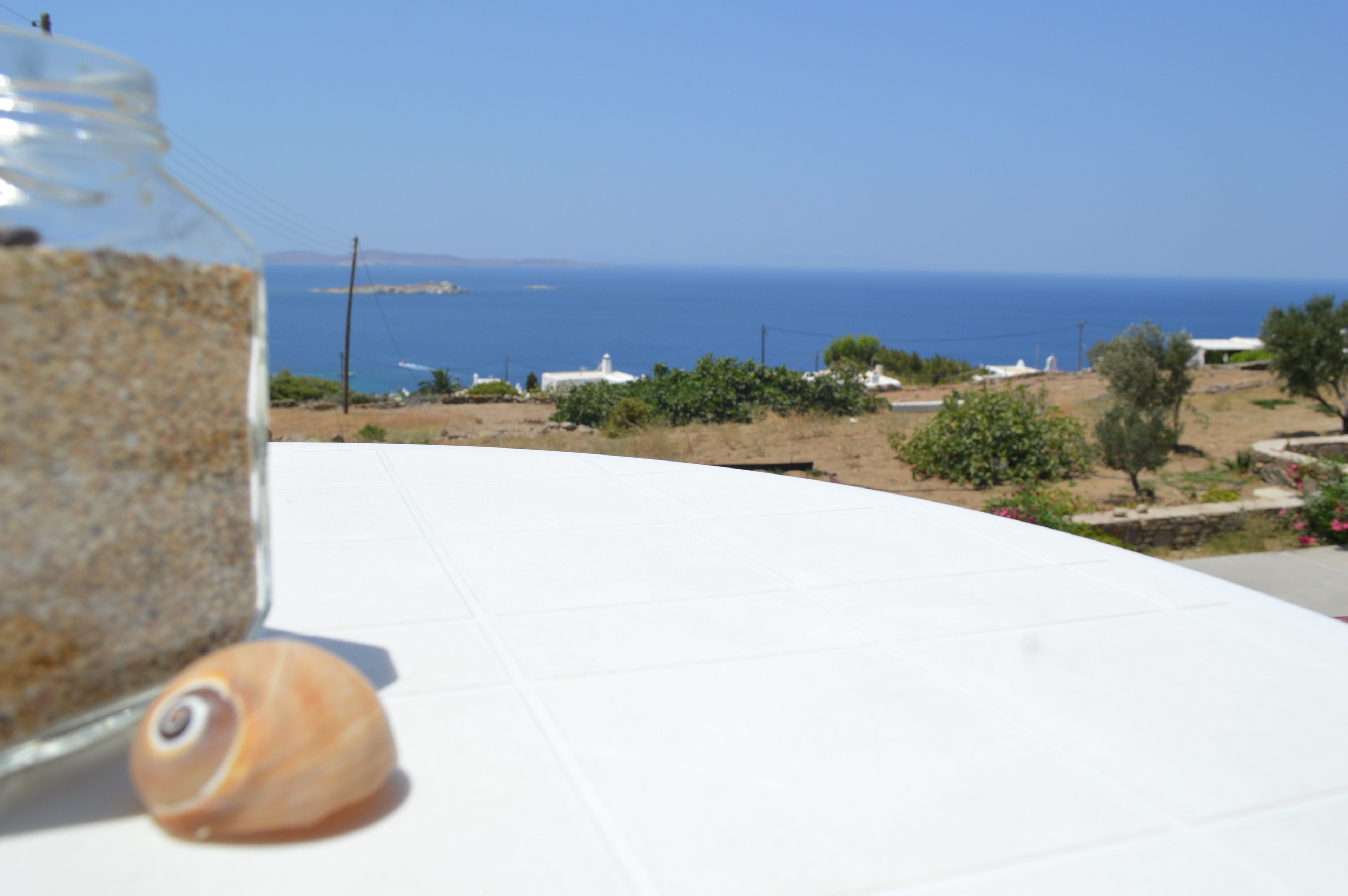 Une table sur laquelle se trouvent un bocal rempli de céréales et un coquillage, avec en toile de fond un paysage côtier comprenant des bâtiments et la mer.