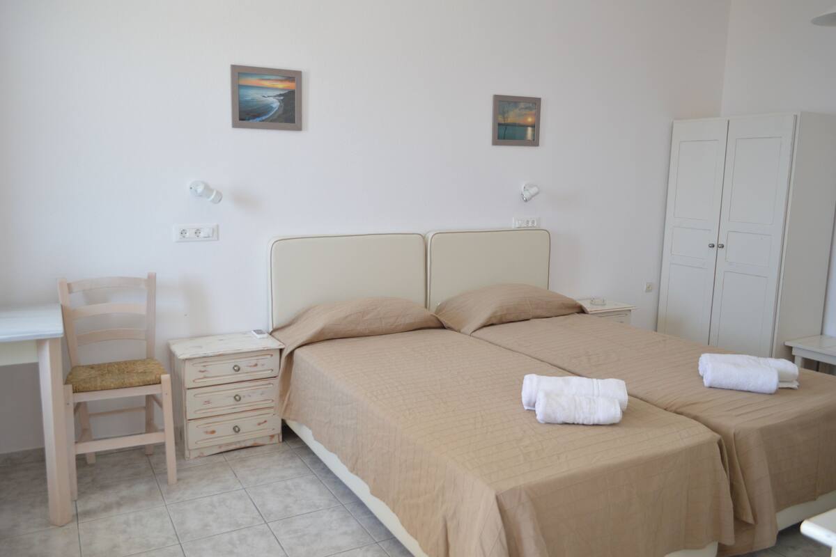 A bedroom with two beds, a desk, a chair, and a wardrobe.