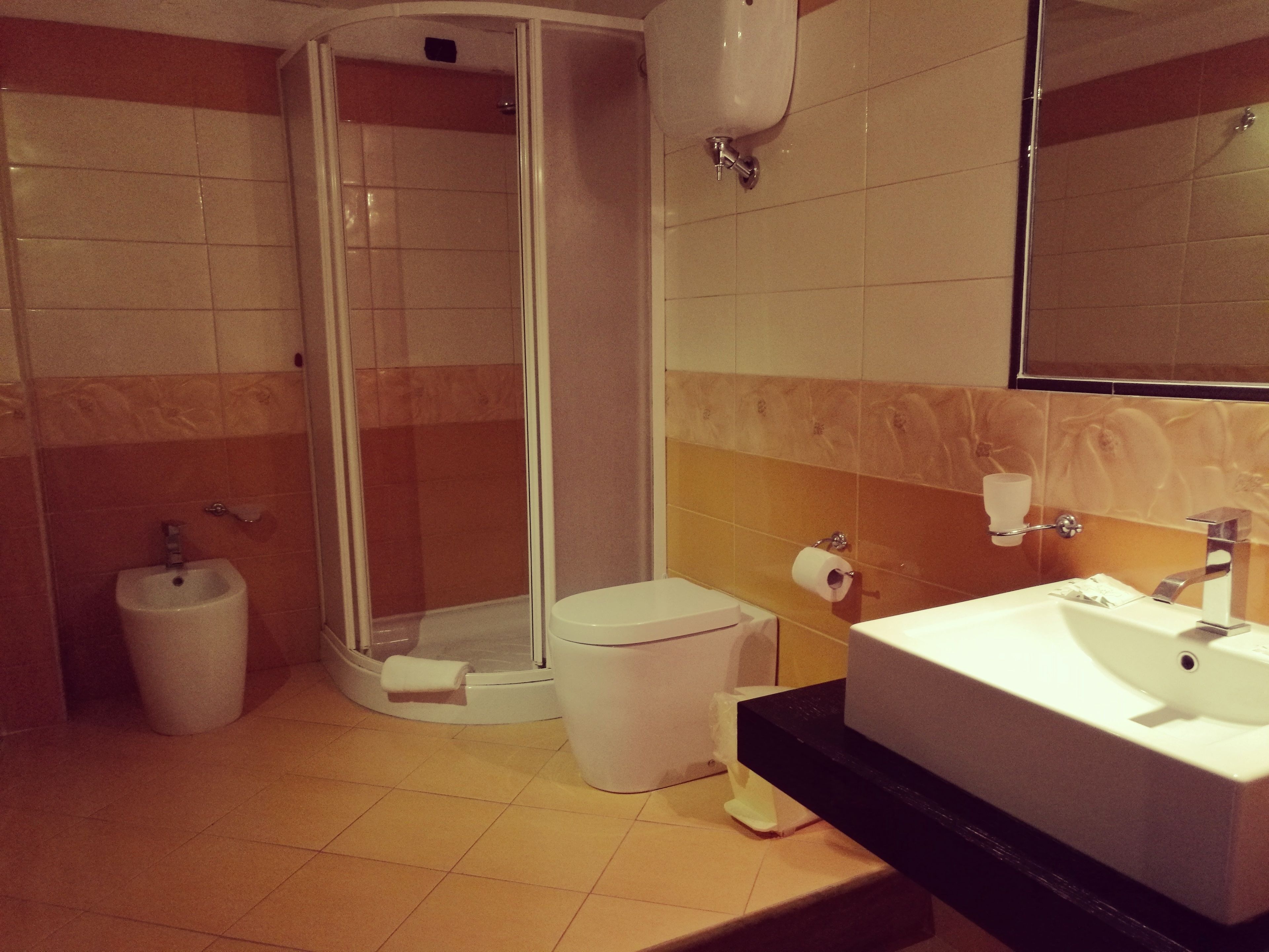 A modern bathroom with a glass-enclosed shower, a pedestal sink, and a toilet.