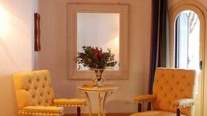 A cozy room with two yellow upholstered chairs, a small round table with a vase of flowers, and a tray with pastries and tea set.