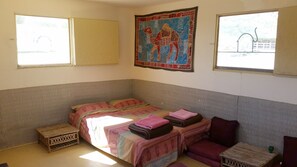 A room with a bed, a small wooden table, a bench, and a tapestry on the wall.