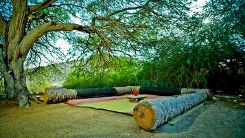 A rustic outdoor seating area with a large log bench, a small table, and a red cup.