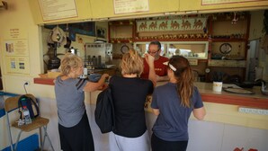 A group of people at a counter in a cafe with a menu board above. - Negev Camel Ranch (Dimona)
