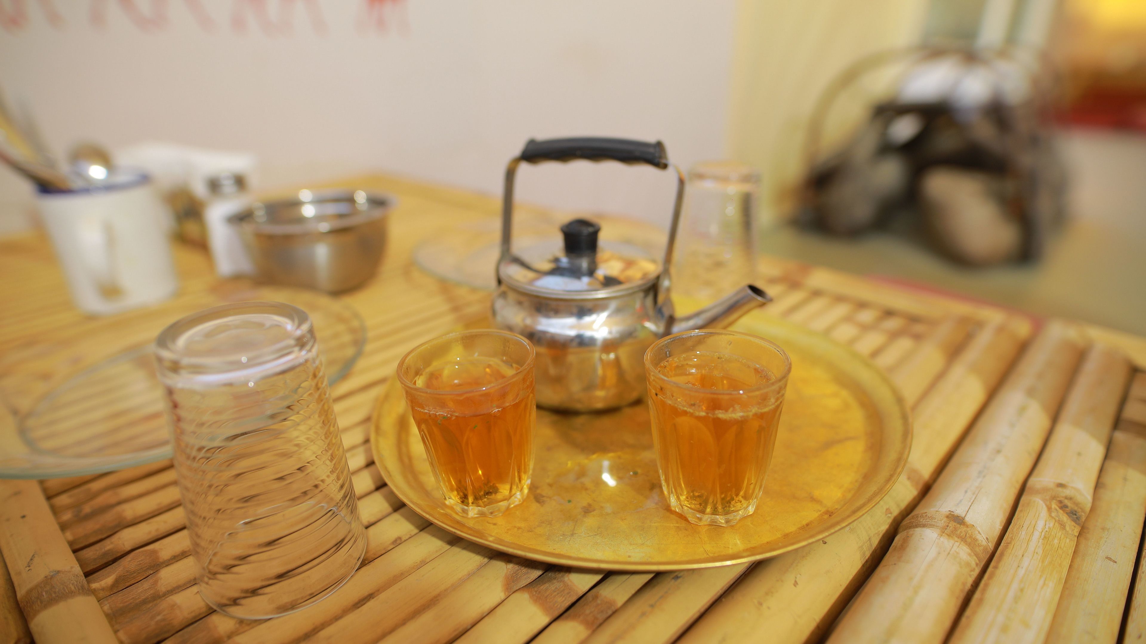 A bamboo table with a tea set including a teapot, two glasses, and a tray.