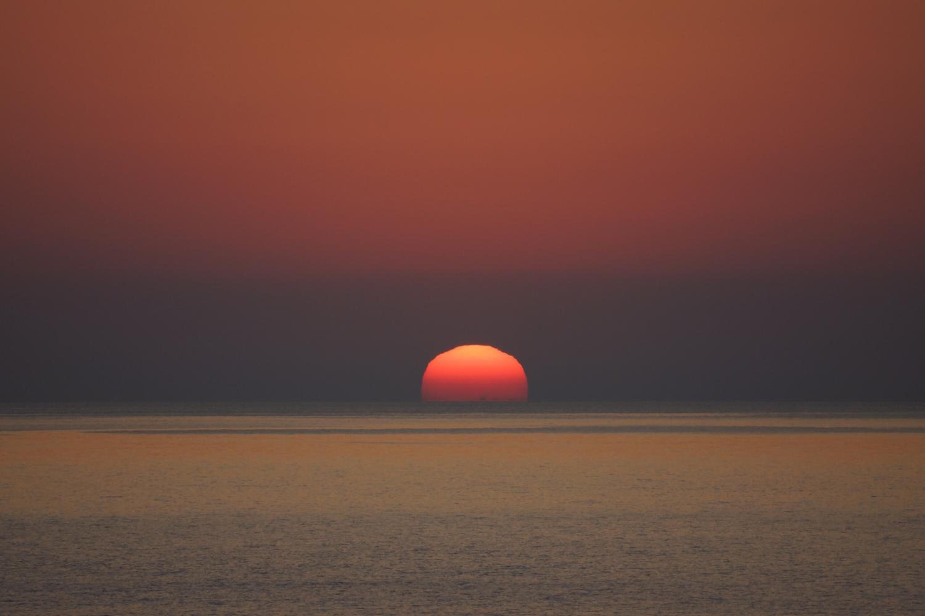 Ein Sonnenuntergang über einem ruhigen Meer mit klarem Horizont.