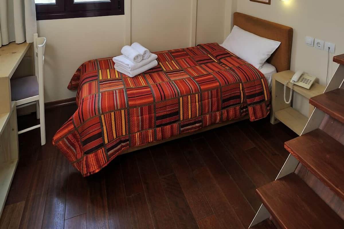 A single bedroom with a bed, a bedside table, a telephone, and a window.