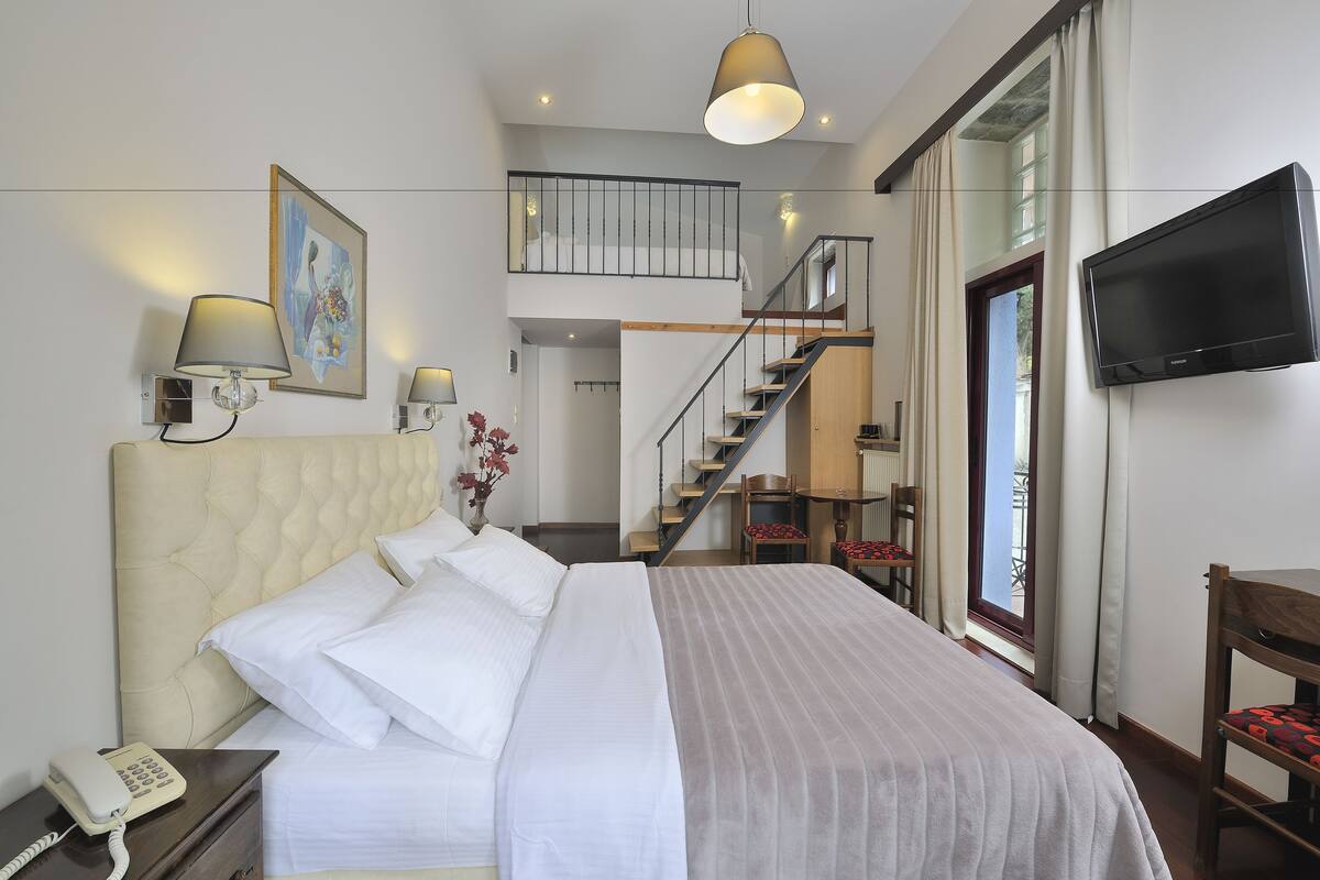 A hotel room with a bed, bedside lamp, phone, TV, and a staircase leading to an upper level.