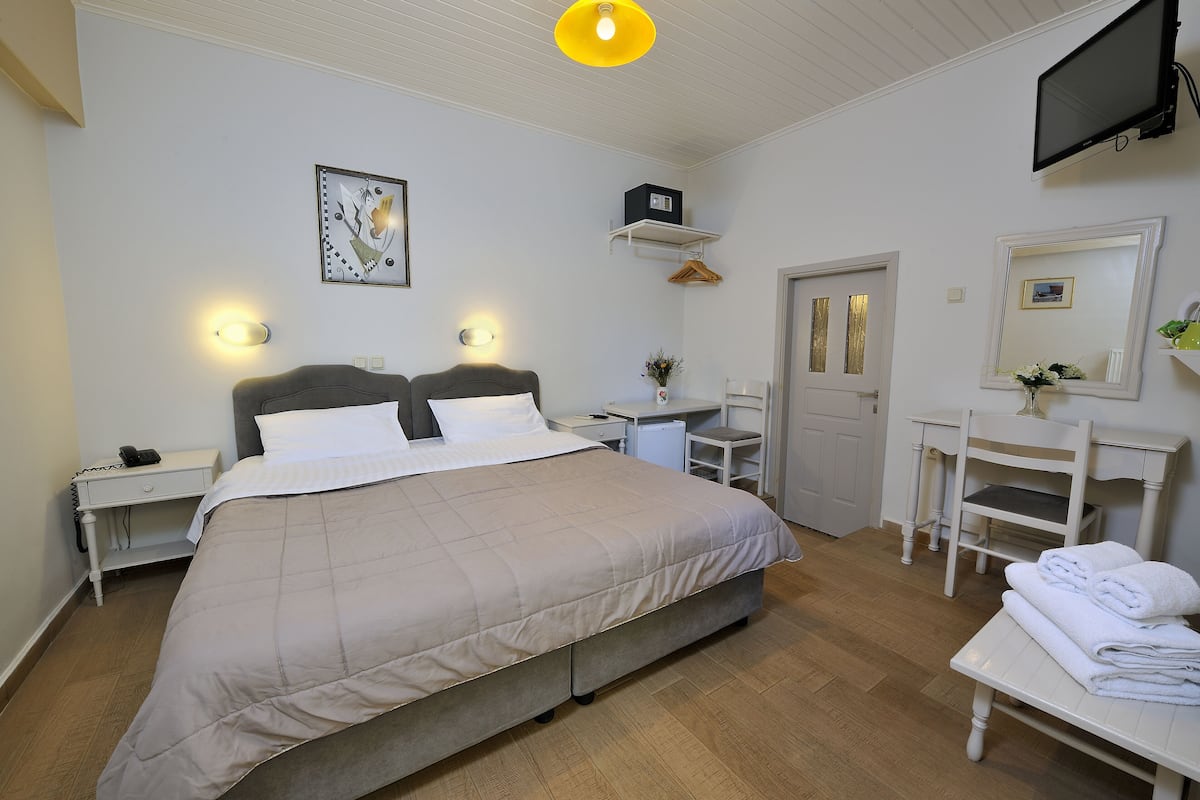 A bedroom with a bed, bedside tables, a desk, a chair, a TV, and a mirror.