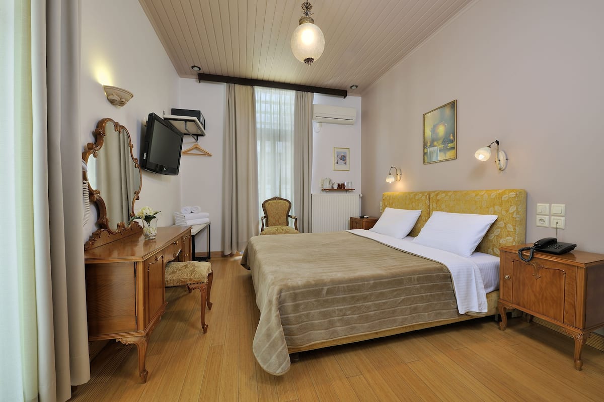 A hotel room with a bed, a wooden dresser, a chair, a desk, a television, and a painting on the wall.