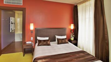Een hotelkamer met een groot bed, twee bedlampen, een nachtkastje, een raam met gordijnen en een deur naar een badkamer.