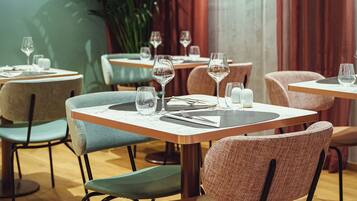 A restaurant interior with round tables, cushioned chairs, and a potted plant.