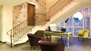 A staircase with a stone wall, a wooden door, and a desk with a chair. - Hotel Le Clos Rebillotte (Luxeuil-les-Bains)
