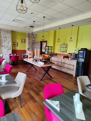 Un restaurante con suelos de madera, sillas rojas y blancas, una mesa central con comida y una máquina de café.