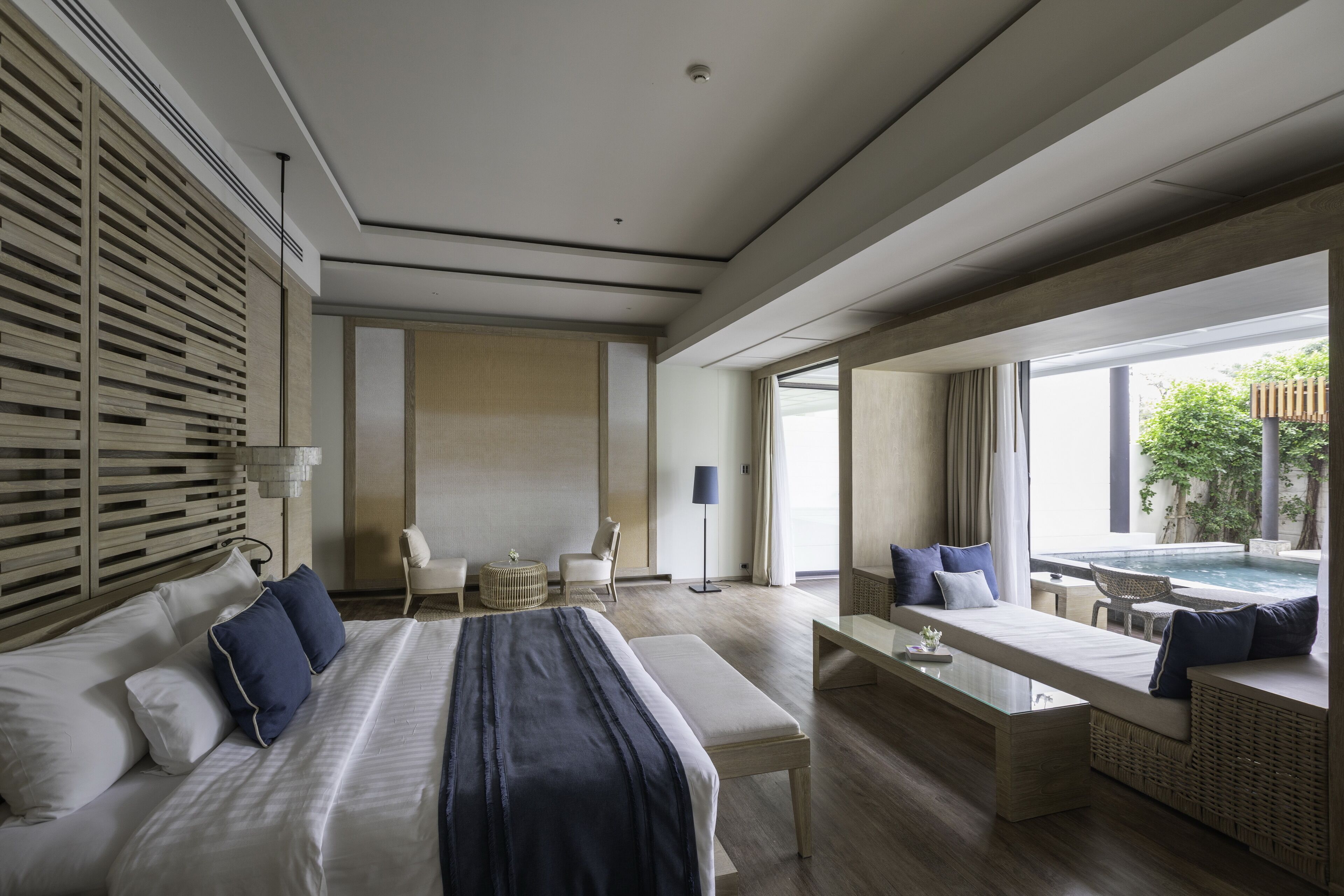 Ein modernes Hotelzimmer mit einem großen Bett, einer Sitzecke mit Blick auf einen Pool und einem Esstisch.