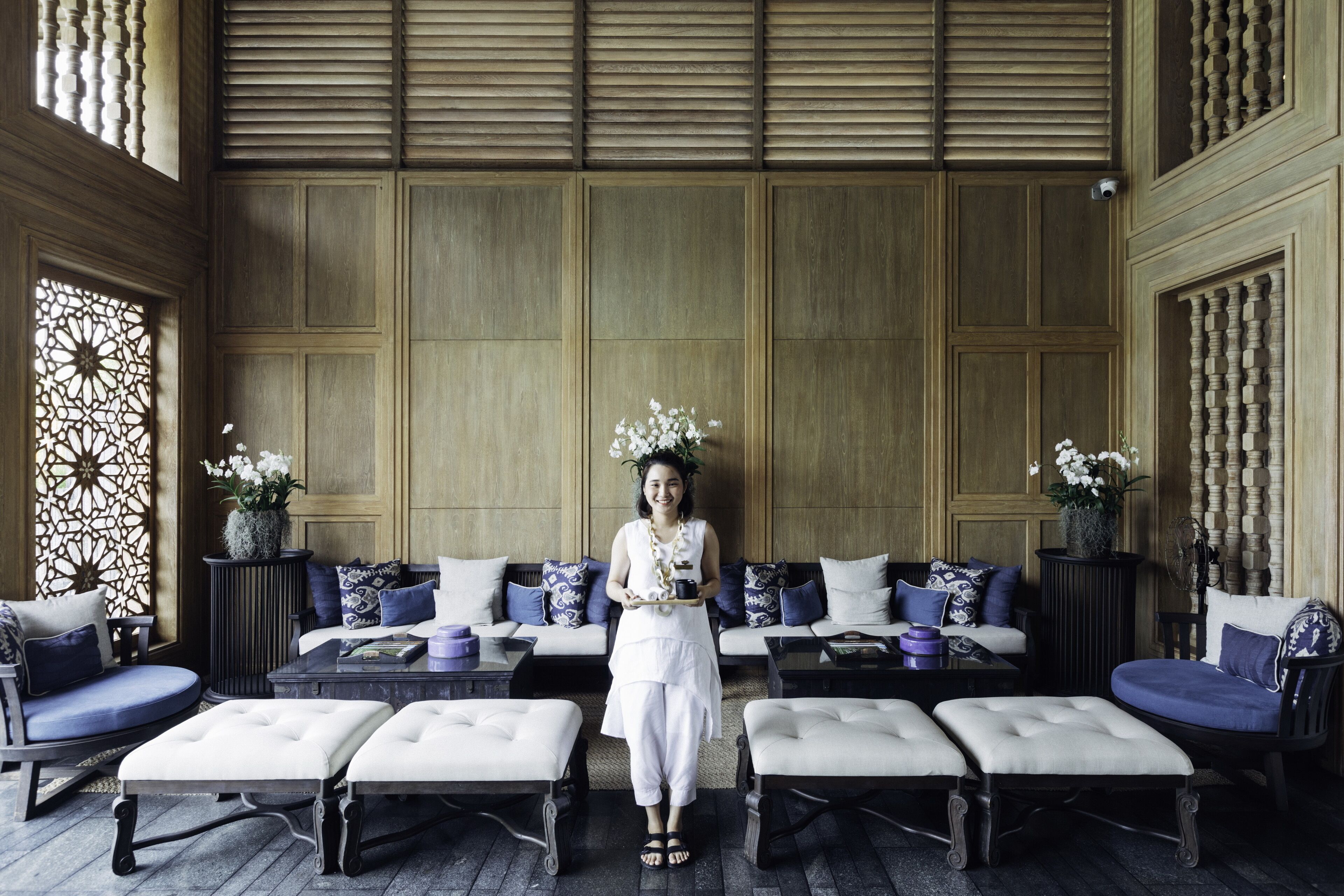 A spacious room with a high ceiling, a seating area with sofas and ottomans, and decorative vases with flowers.