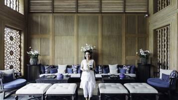 A spacious room with a high ceiling, a seating area with sofas and ottomans, and decorative vases with flowers.