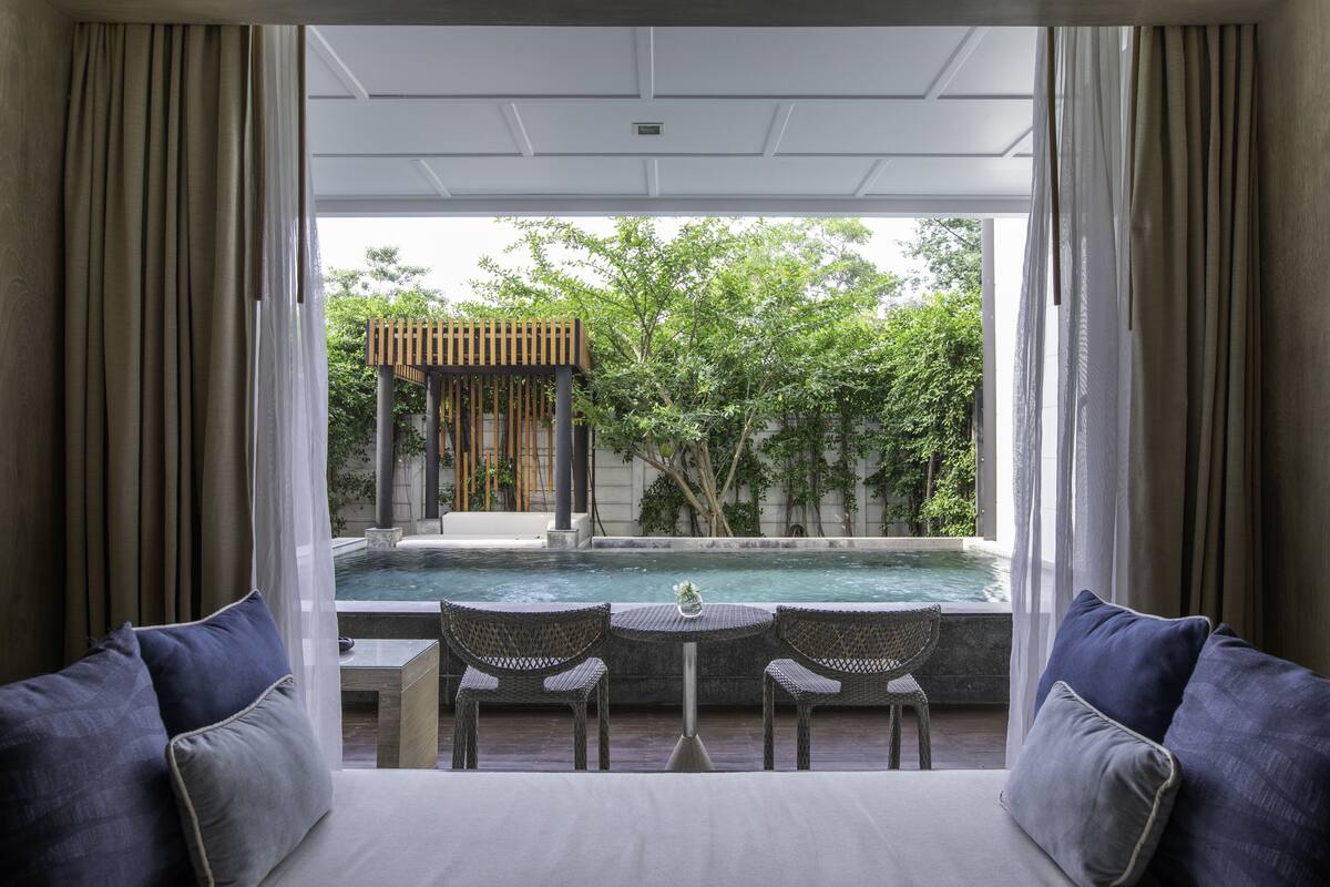 A room with a view of a swimming pool, two wicker chairs, and a small table.