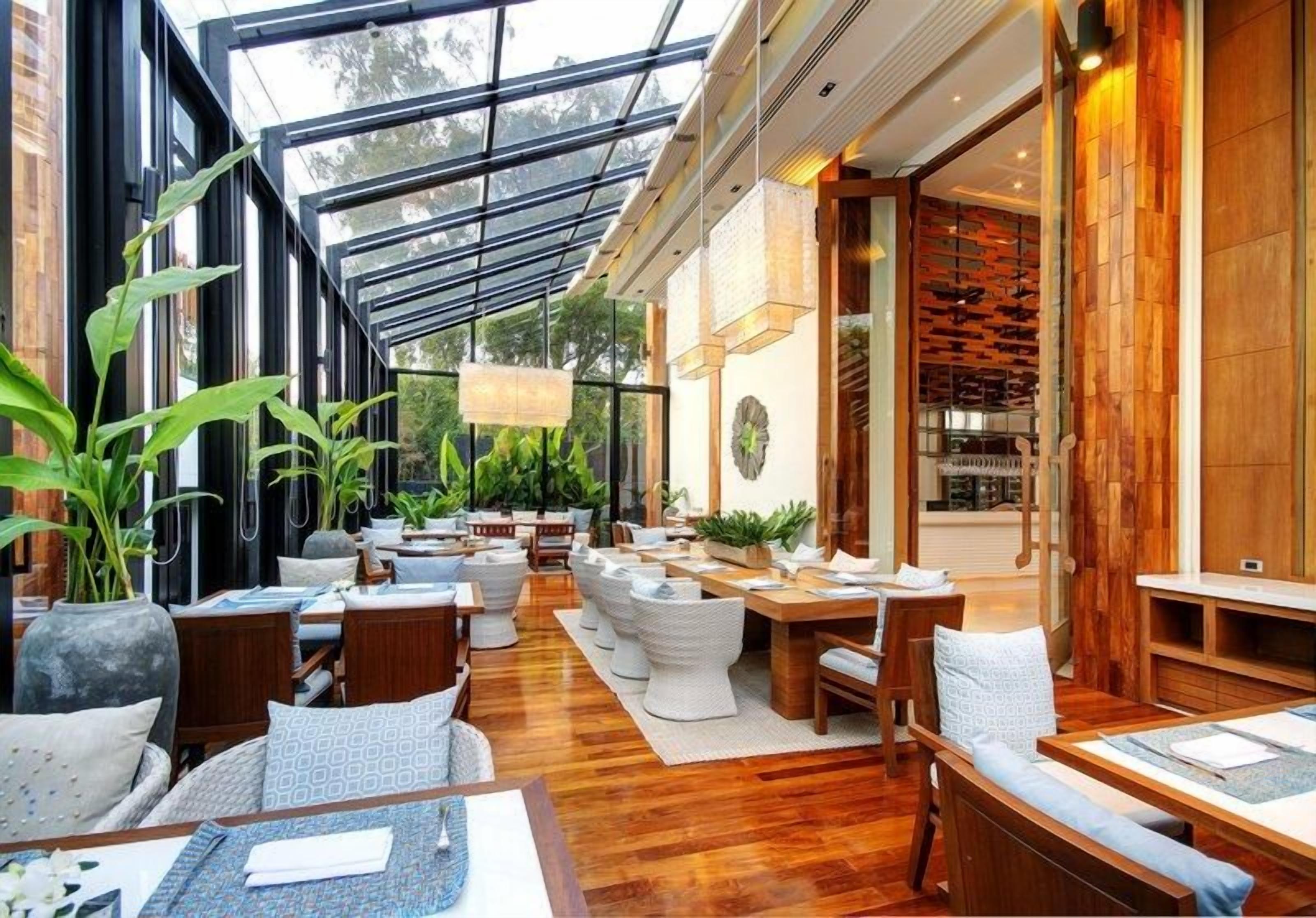 A spacious indoor area with multiple seating arrangements, including tables and chairs, under a glass ceiling.