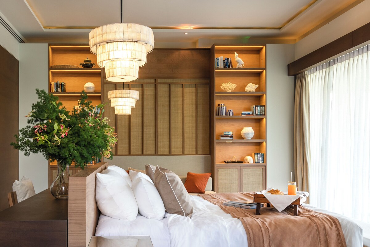 A modern bedroom with a bed, bedside tables, a bookshelf, and a large window with curtains.