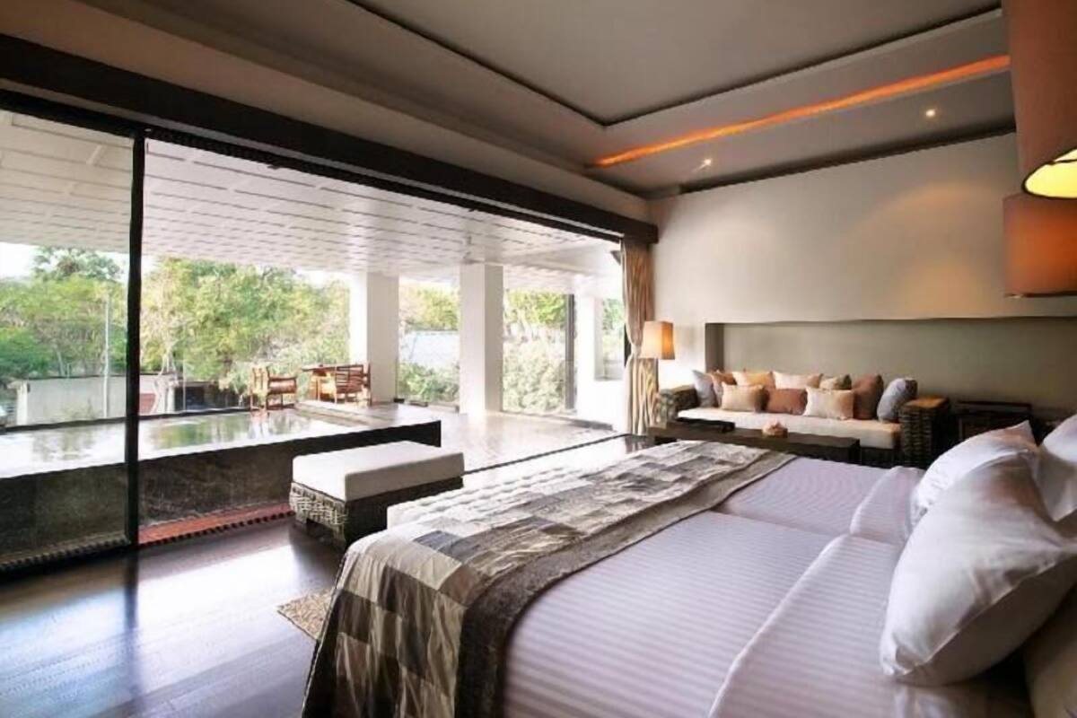 A modern bedroom with a large bed, a sofa, and a view of greenery outside.