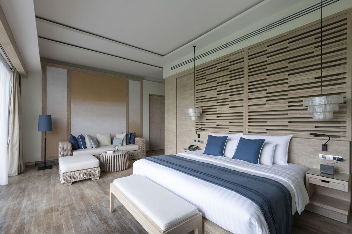 A modern bedroom with a large bed, a sofa, a bench, and a small table.