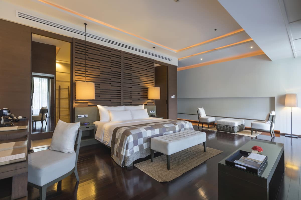 A modern hotel room with a large bed, a desk, a chair, and a sofa.