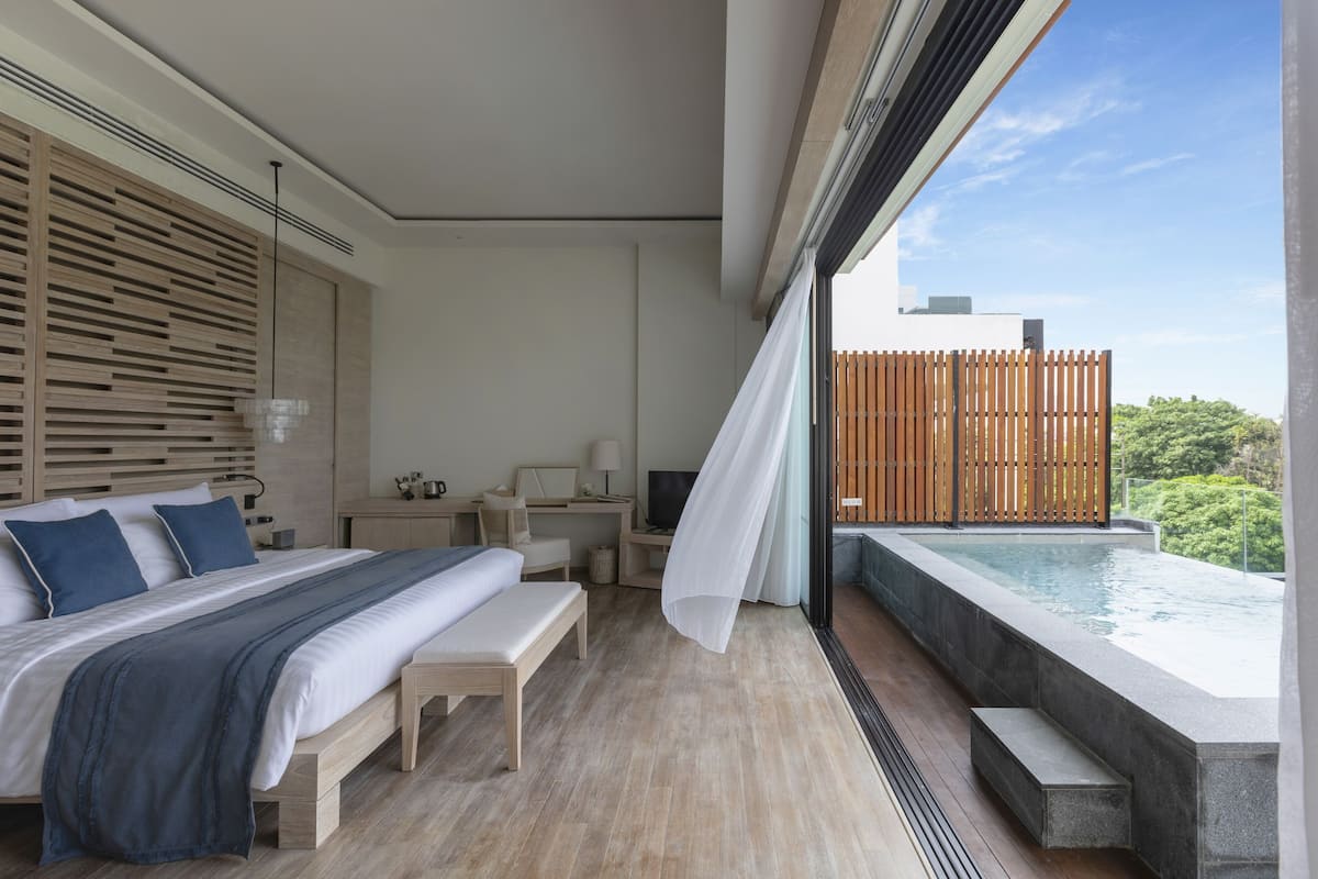 A modern bedroom with a large bed, bedside tables, a desk, and a view of a swimming pool.