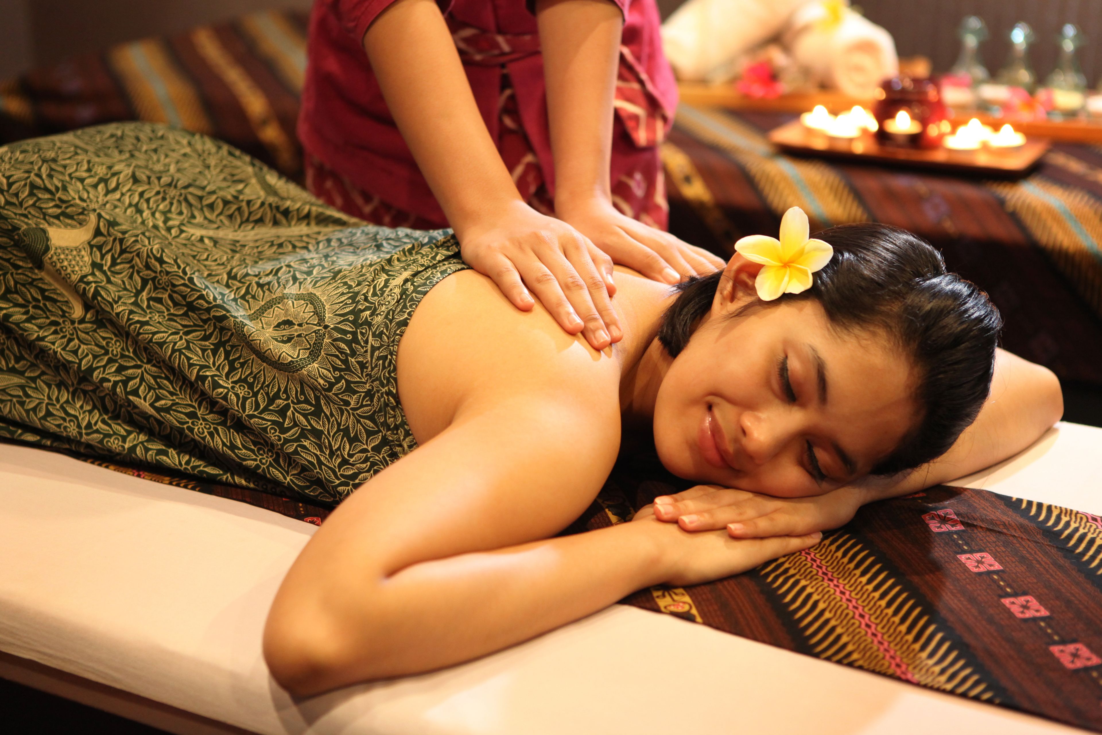 A massage therapy session in a room with a patterned bedspread and a tray of candles in the background.