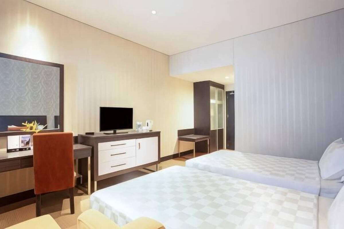 A hotel room with a bed, a desk with a TV, a chair, and a mirror.