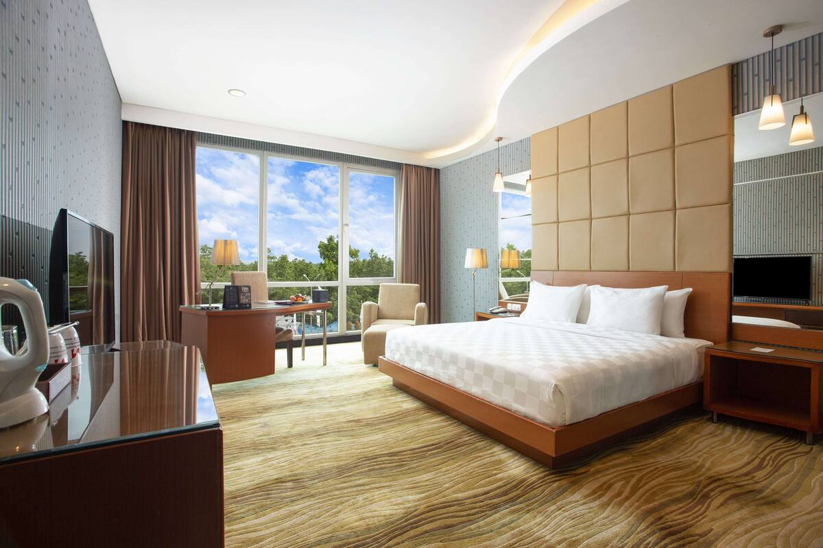 A hotel room with a large bed, a desk with a television, a chair, and a view of the outdoors.