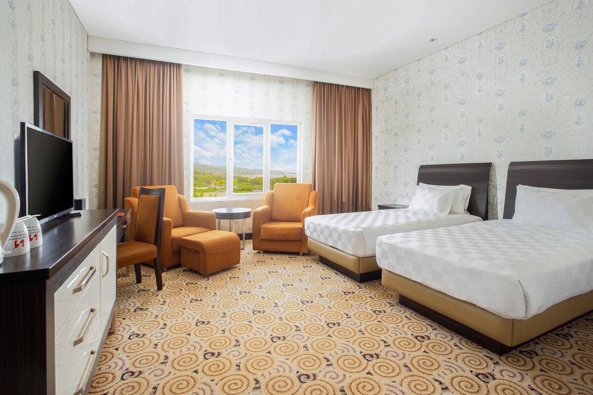A hotel room with two beds, a TV, a desk, and a view of the outdoors.