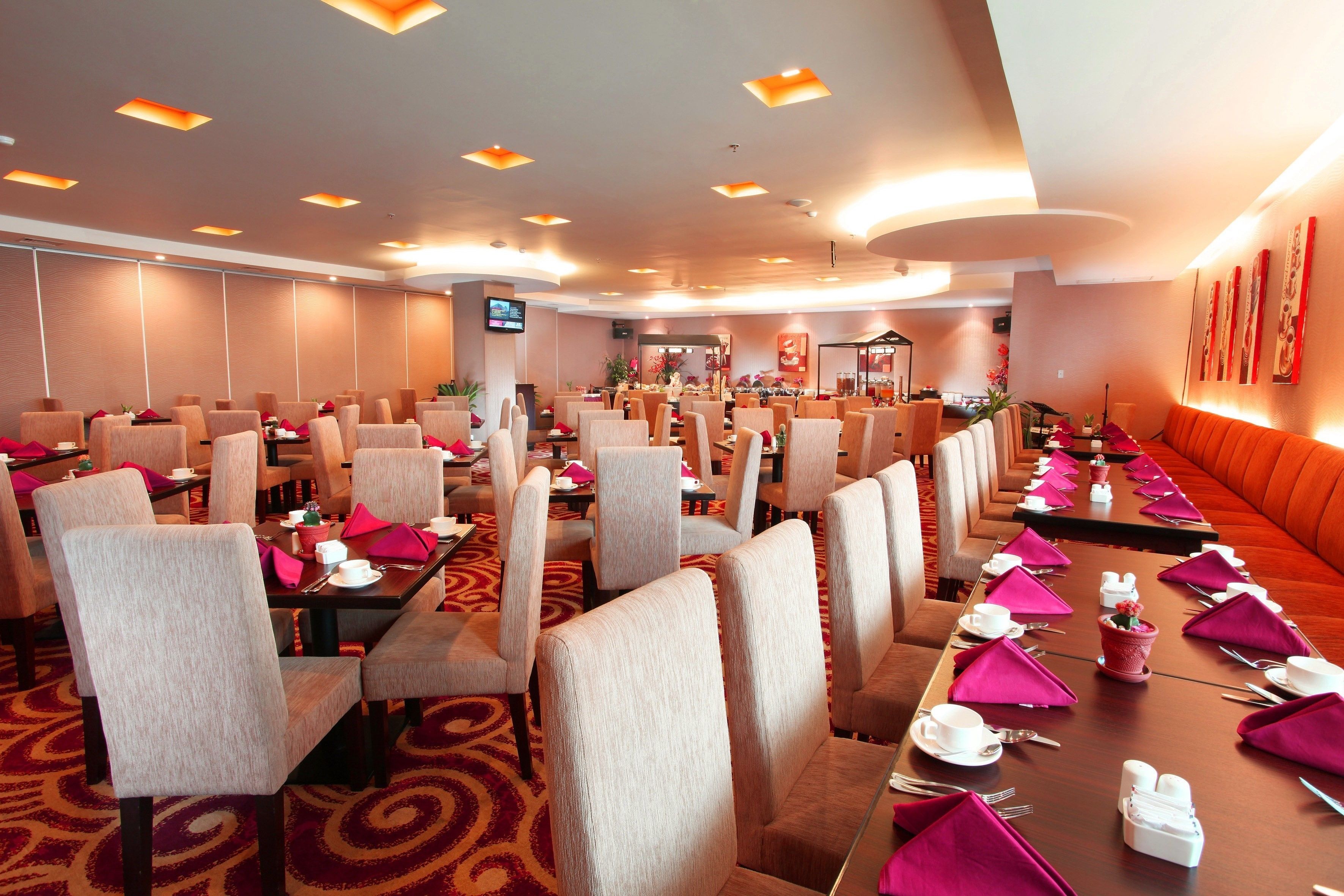 A hotel dining area with multiple tables and chairs, equipped with table settings and a television screen.