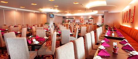 A hotel dining area with multiple tables and chairs, equipped with table settings and a television screen.