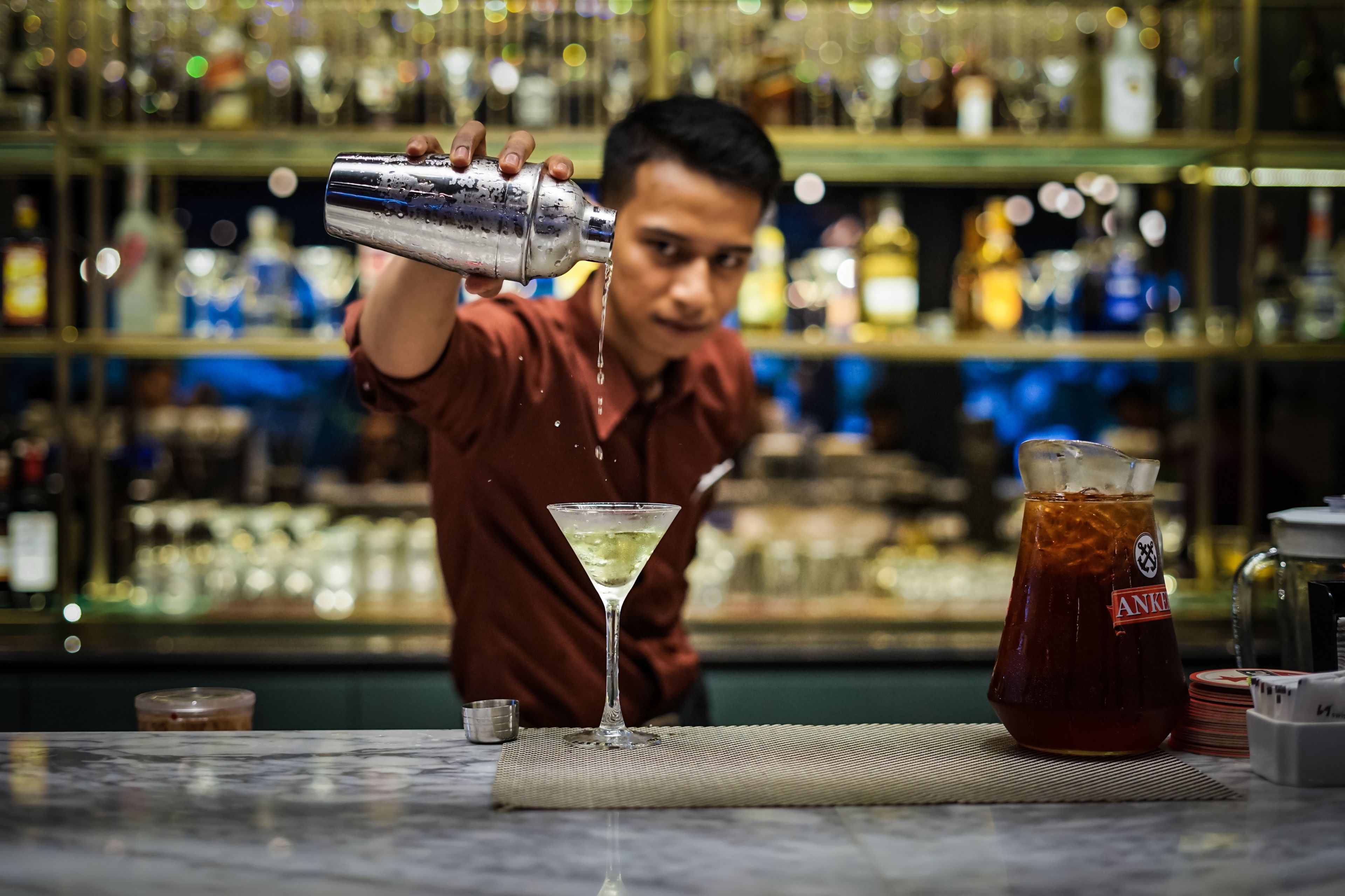 Ein Barkeeper gießt ein Getränk in ein Martini-Glas.