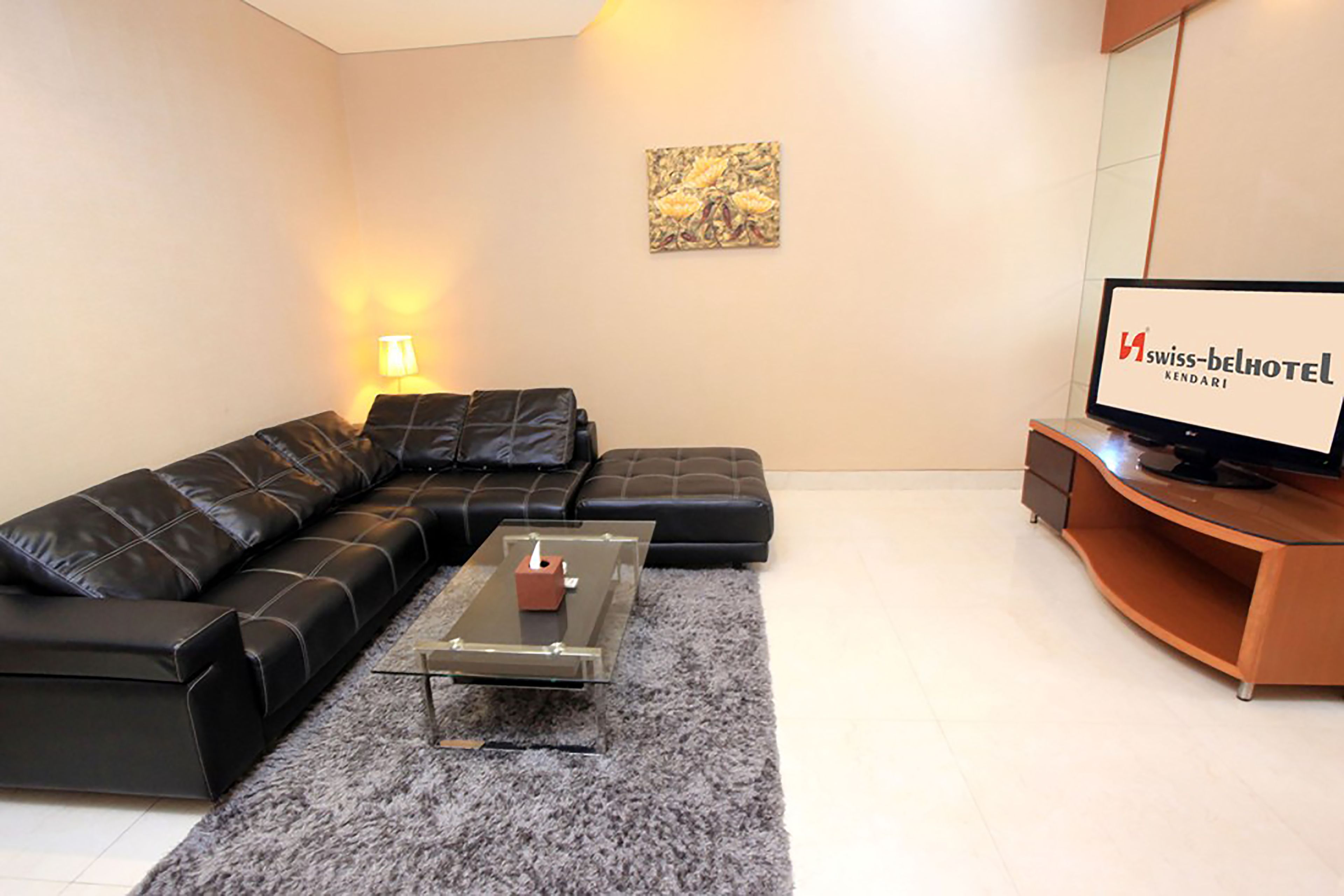 Una sala de estar moderna con un sofá de cuero negro, una mesa de centro de vidrio y un televisor de pantalla plana sobre un pedestal de madera.