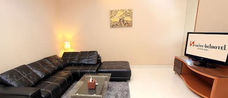 A modern living room with a black leather sofa, a glass coffee table, and a flat-screen TV on a wooden stand.