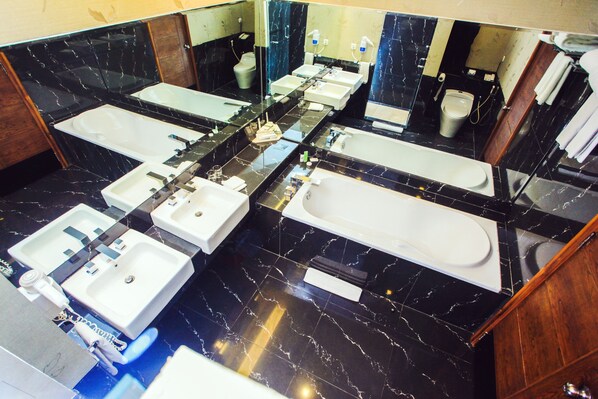 A bathroom with multiple sinks, a bathtub, and a large mirror. - Swiss-Belhotel Kendari (Kendari)