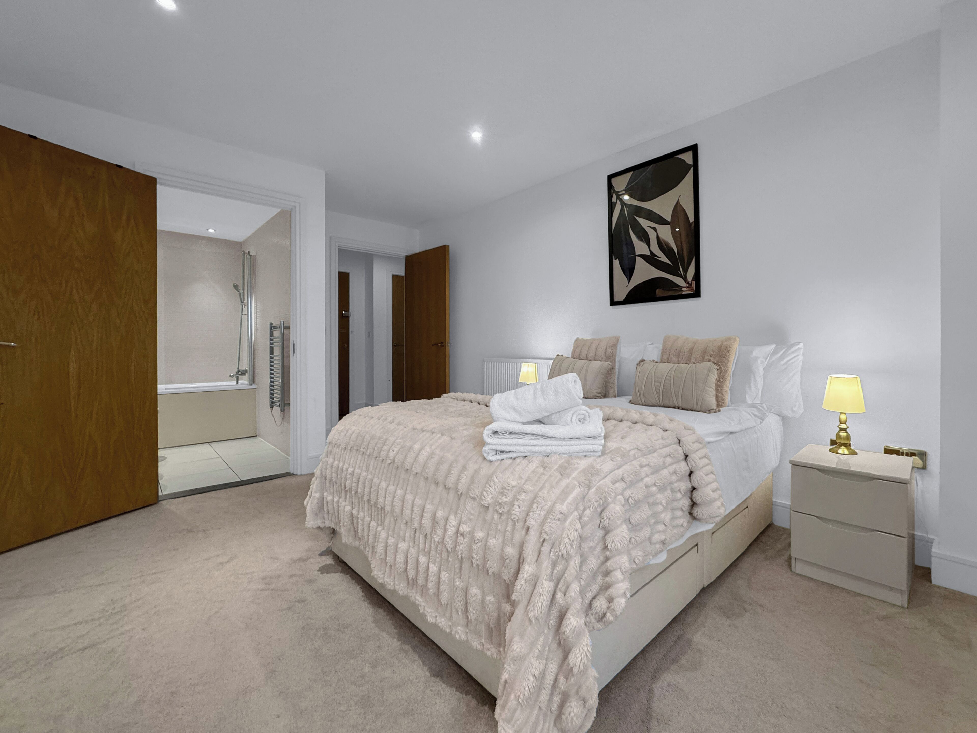 A bedroom with a large bed, a bedside table with a lamp, a wooden wardrobe, and a bathroom with a shower.