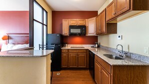 A compact kitchen with wooden cabinets, a microwave, a sink, and a refrigerator. - Comfort Suites Lake Worth (Fort Worth)