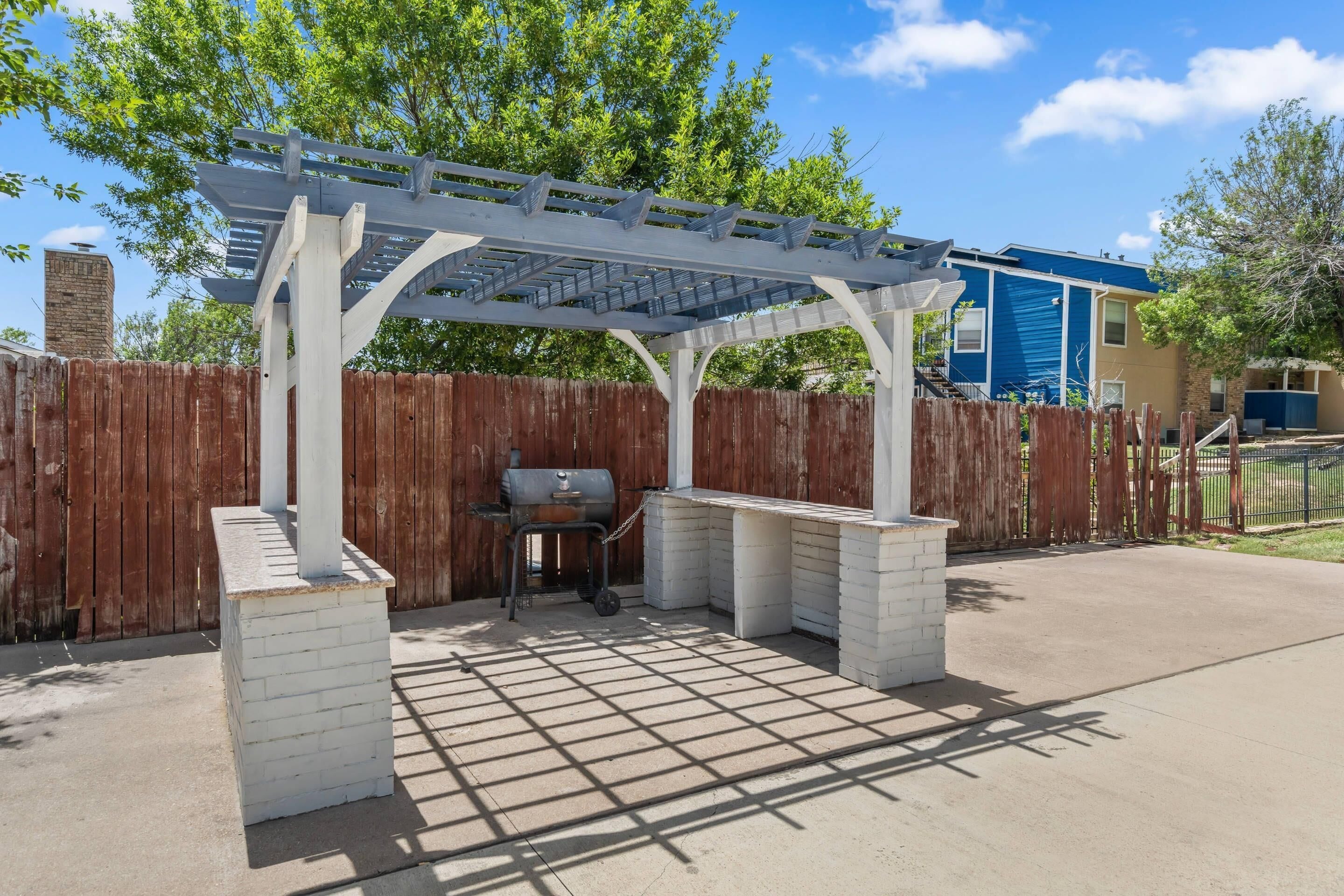 Eine Außenpatio mit Pergola, Grill und Barbereich aus Ziegeln.