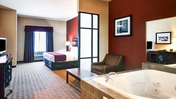 A hotel room with a bed, a chair, a desk, a TV, a large window, and a bathtub. - Comfort Suites Lake Worth (Fort Worth)