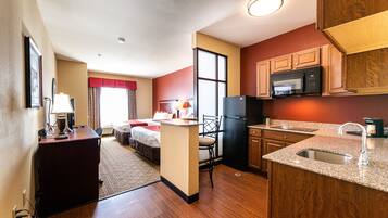A compact hotel room with a kitchenette, a bed, a desk, and a chair.