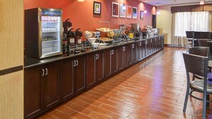 A breakfast bar with a refrigerator, coffee machines, and a variety of food items. - Comfort Suites Lake Worth (Fort Worth)