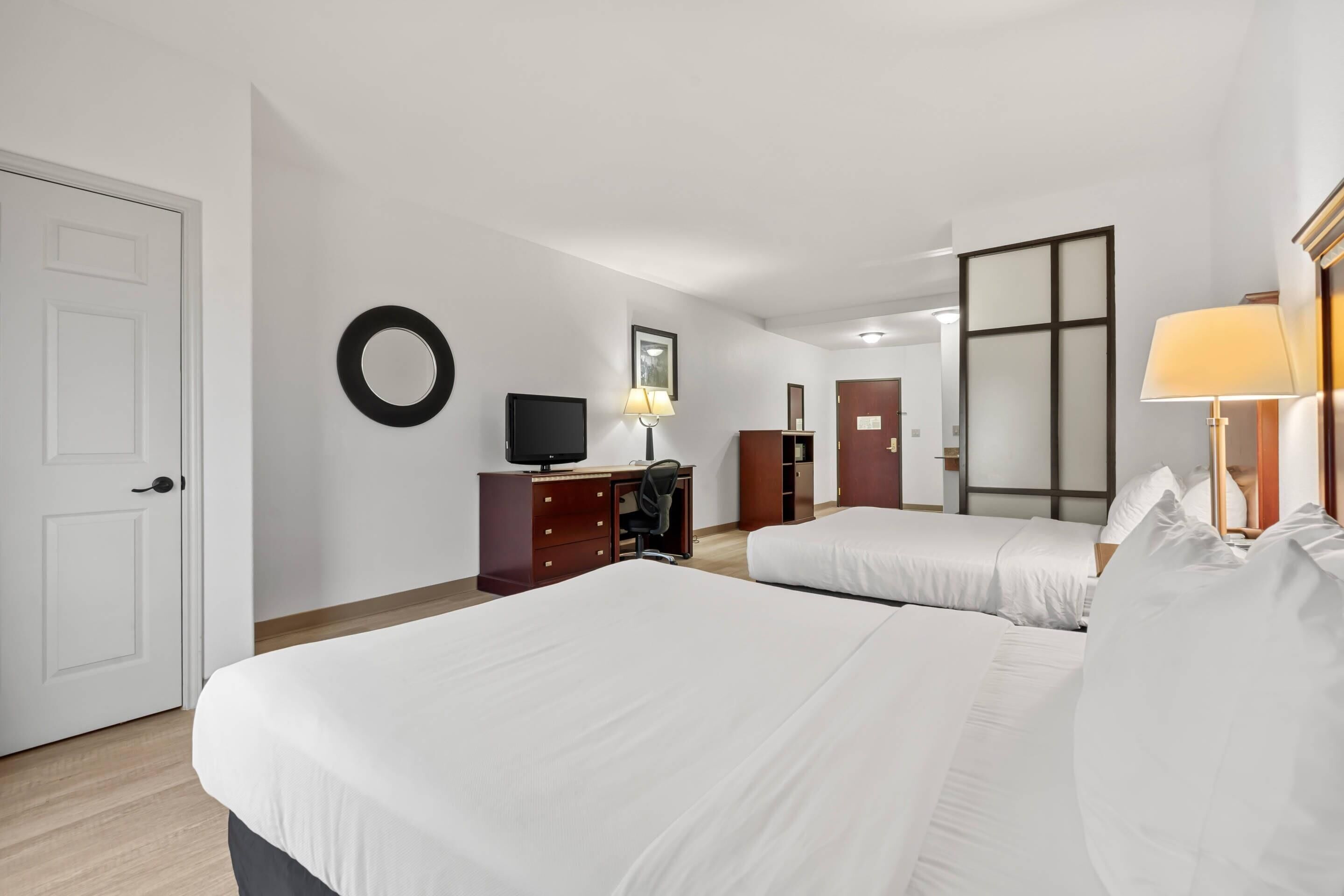 Una camera d'albergo con due letti, una scrivania con un computer, una televisione e uno specchio.