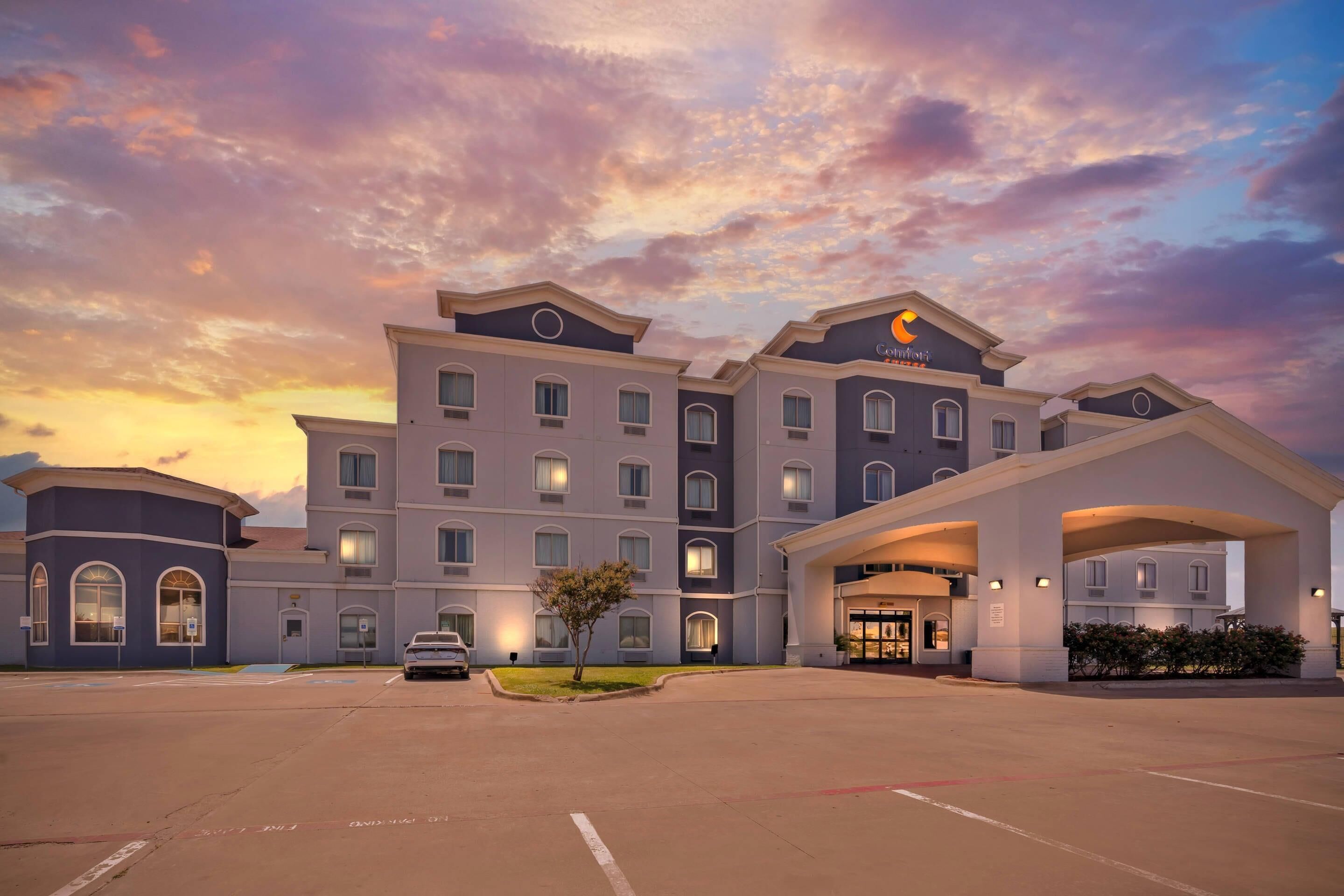 A hotel with a central entrance, multiple floors, and a parking lot.