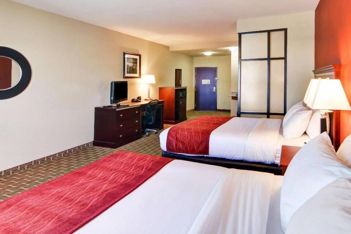 Ett hotellrum med två sängar, ett skrivbord, en stol, en tv och en dörr.